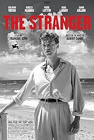 Movie poster for The Stranger, a film by François Ozon based on the novel by Albert Camus, showing a man standing on a beach in a black and white scene`